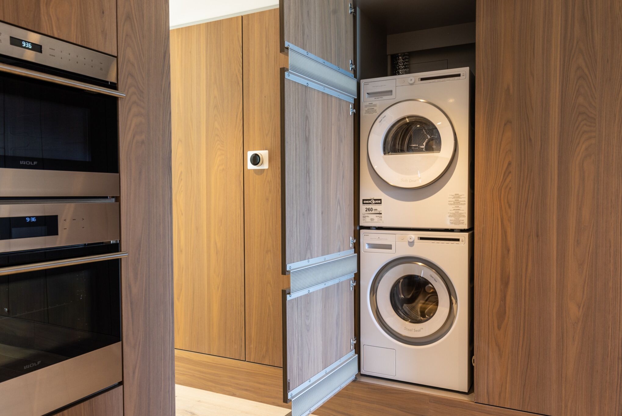 A compact laundry room with a front-loading washer and dryer, built-in oven, and a wooden cabinet.