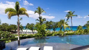 Un espace piscine avec des chaises longues, des palmiers et une vue sur la plage.