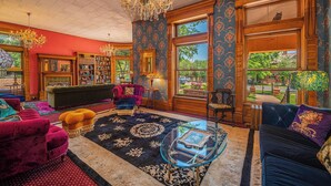 A spacious room with a large window, a chandelier, a fireplace, and a collection of bookshelves. - Orman Mansion - Pueblo's Most Luxurious Stay (Pueblo)