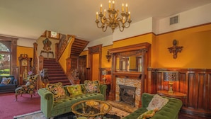 A grand living room with a green sofa, a fireplace, a staircase, and a chandelier. - Orman Mansion - Pueblo's Most Luxurious Stay (Pueblo)