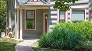 A house with a front porch, a pathway leading to the entrance, and a well-maintained lawn with tall grass.