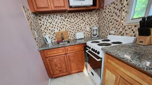 A compact kitchen with wooden cabinets, a white stove, a microwave, and a coffee maker. - Periwinkle - Upscale Studio w Pool Near Beach
 (Nassau)