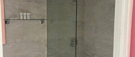 Une salle de bain avec une douche à parois de verre, des toilettes et une étagère contenant des articles de toilette.