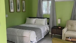 A bedroom with a bed, a chair, a nightstand, and a window with curtains. - Green Turtle - Upscale Studio w Pool Near Beach
 (Nassau)