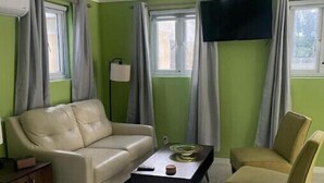 A room with a bed, a beige sofa, a small table with a lamp, and a television mounted on the wall. - Green Turtle - Upscale Studio w Pool Near Beach
 (Nassau)