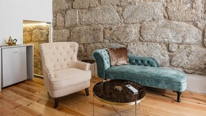 A room with a stone wall, a beige armchair, a teal sofa, and a small table with a remote control. - GuestReady - Boutique style loft in Constituição (Porto)