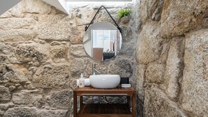 A stone-walled bathroom with a wooden vanity, a round mirror, and a hanging plant. - GuestReady - Boutique style loft in Constituição (Porto)