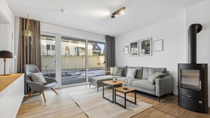A modern living room with a sofa, a coffee table, a fireplace, and a view through large windows. - GebirgsResort Winterberg (Winterberg)