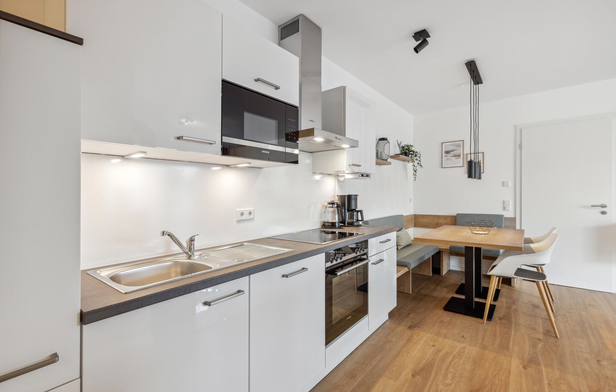 Eine moderne Küche mit Einbauofen, Mikrowelle und Spüle. Es gibt einen Essbereich mit einem Holztisch und Stühlen.