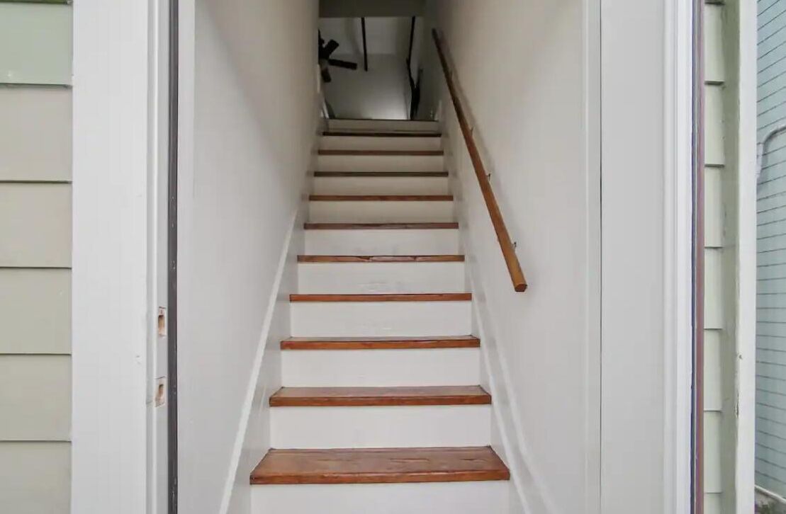 Una escalera estrecha con escalones de madera y barandilla, que lleva a un piso superior.