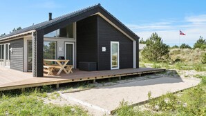 A modern beach house with a wooden deck, a dining area, and a large window. - Lovely home in Ringkøbing with kitchen (Ringkøbing)