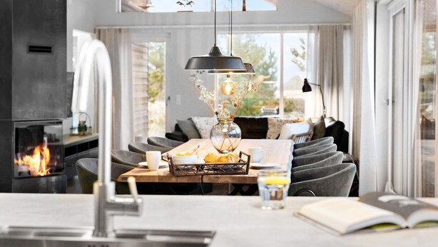 A cozy dining area with a fireplace, a table set with bread, a vase with flowers, and a book. - Lovely home in Ringkøbing with kitchen (Ringkøbing)