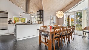 A modern kitchen with a central island, wooden dining table with chairs, and large windows offering views of the outdoors. - Gorgeous home in Glesborg with WiFi (Glesborg)