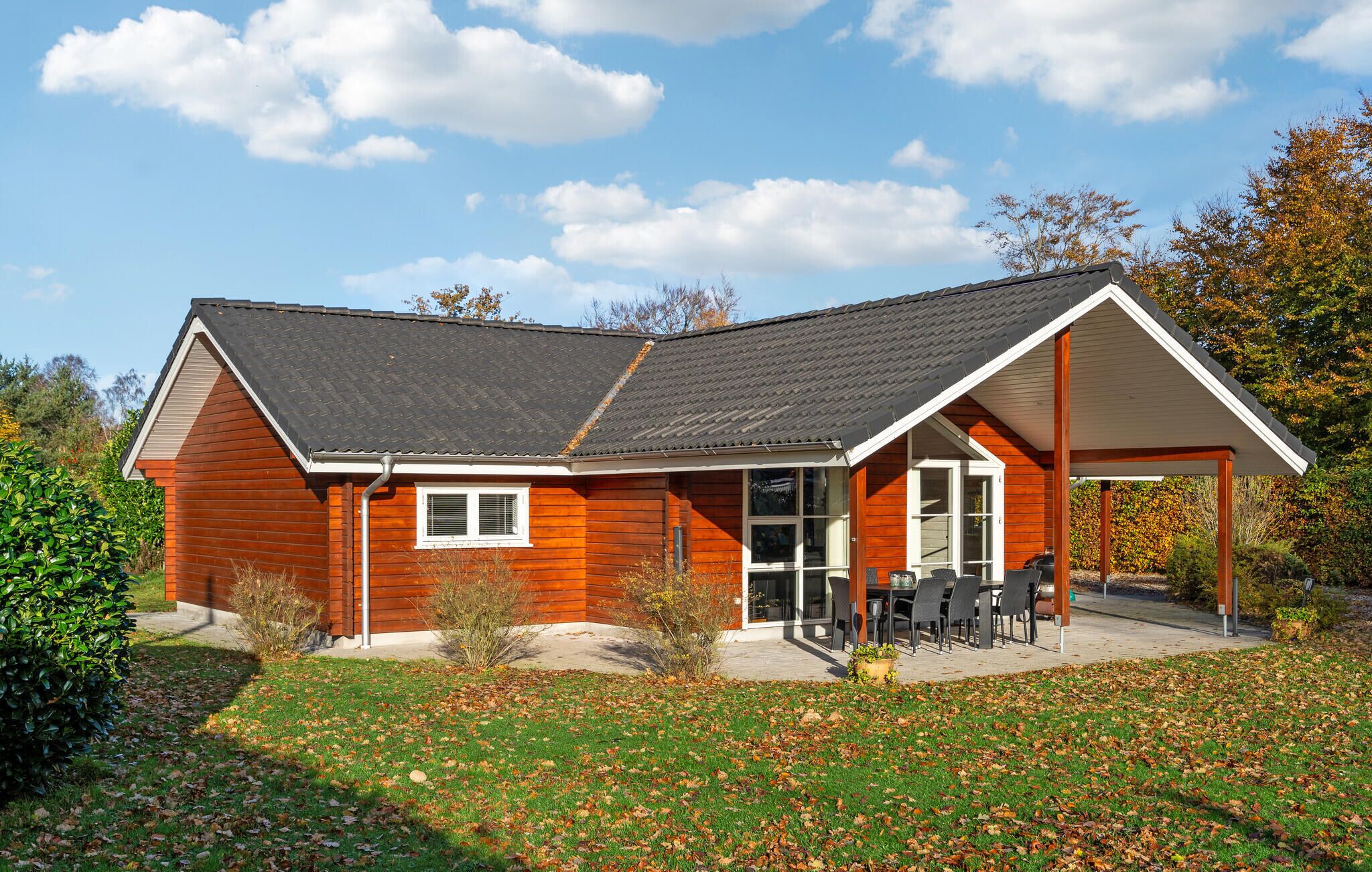 Een houten huis met een schuin dak, een overdekte patio met buitenmeubilair en een verzorgd gazon.