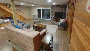 A spacious living room with a wooden floor, a sofa set, a coffee table, and a TV. - The Getaway Cabin W/ Indoor hot tub and sauna.
 (Alger)