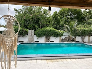 A swimming pool with a clear blue water, surrounded by a white wall and lush greenery.