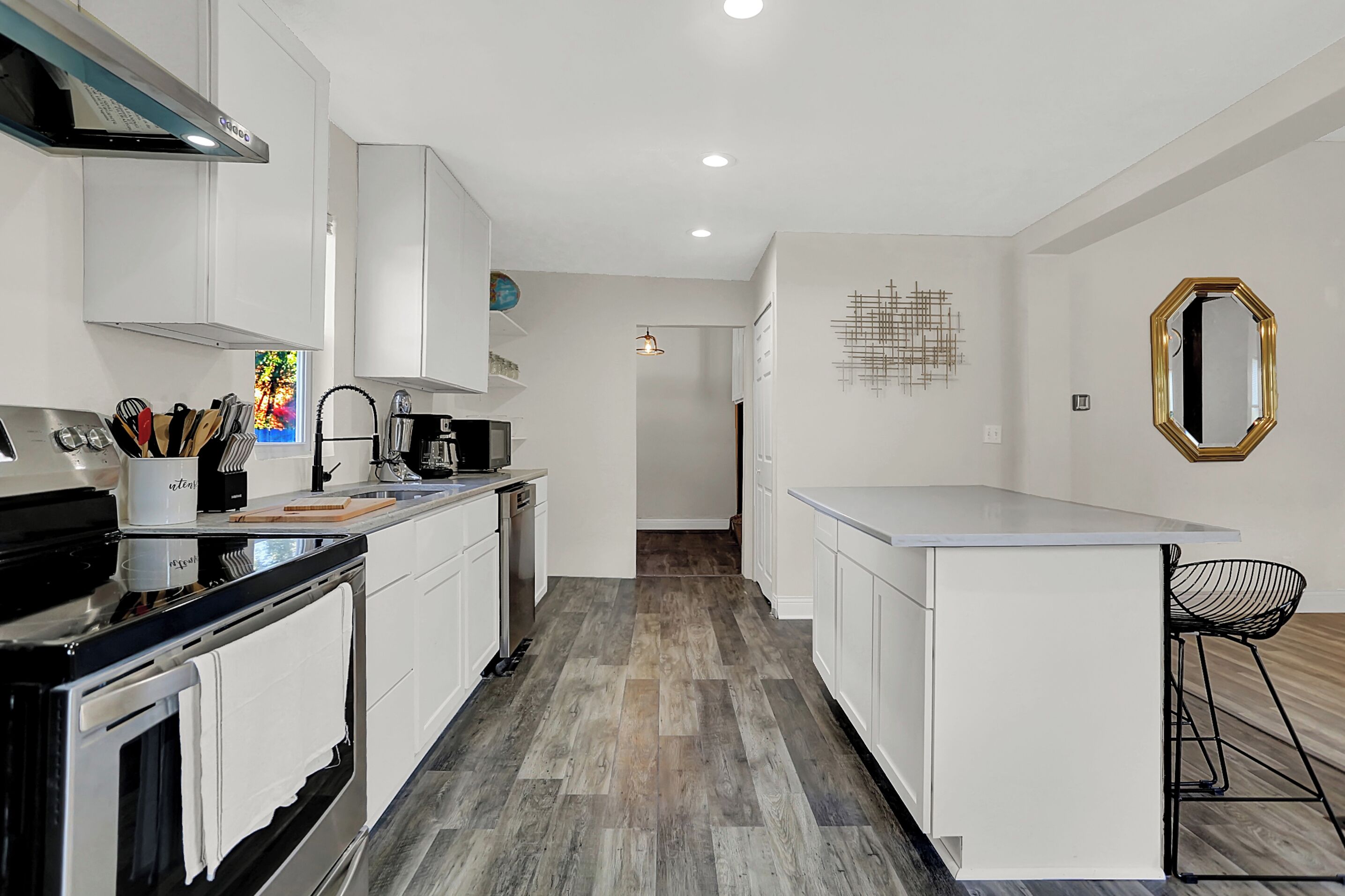 Una cocina moderna con armarios blancos, una estufa negra y piso de madera.