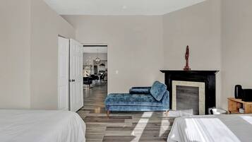 A modern hotel room with two beds, a blue sofa, a fireplace, and a dining area in the background.