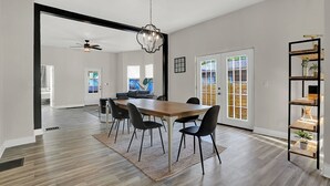 A dining area with a wooden table and black chairs, a chandelier, and a black-framed bookshelf with plants. - Beautiful 3500 SqFt Villa in Fountain Sq (Indianapolis)