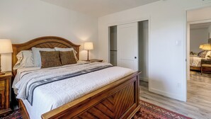 Un dormitorio con una cama de madera, dos lámparas de noche, un tapete estampado y una puerta que da a otra habitación.