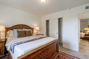 Un dormitorio con una cama de madera, dos lámparas de noche, un tapete estampado y una puerta que da a otra habitación.