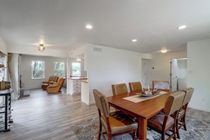 Un comedor amplio con una mesa de madera y sillas de cuero, una cocina al fondo y vistas al exterior a través de ventanas grandes.