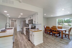 Una cocina moderna con armarios blancos, electrodomésticos de acero inoxidable y un comedor con sillas y mesa de madera.