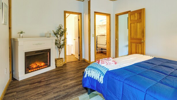 A bedroom with a fireplace, wooden floors, a bed with a blue blanket, and two doors leading to other rooms.