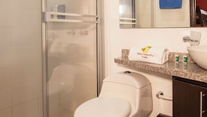 Une salle de bain avec une douche à parois de verre, des toilettes, un lavabo et une poubelle.