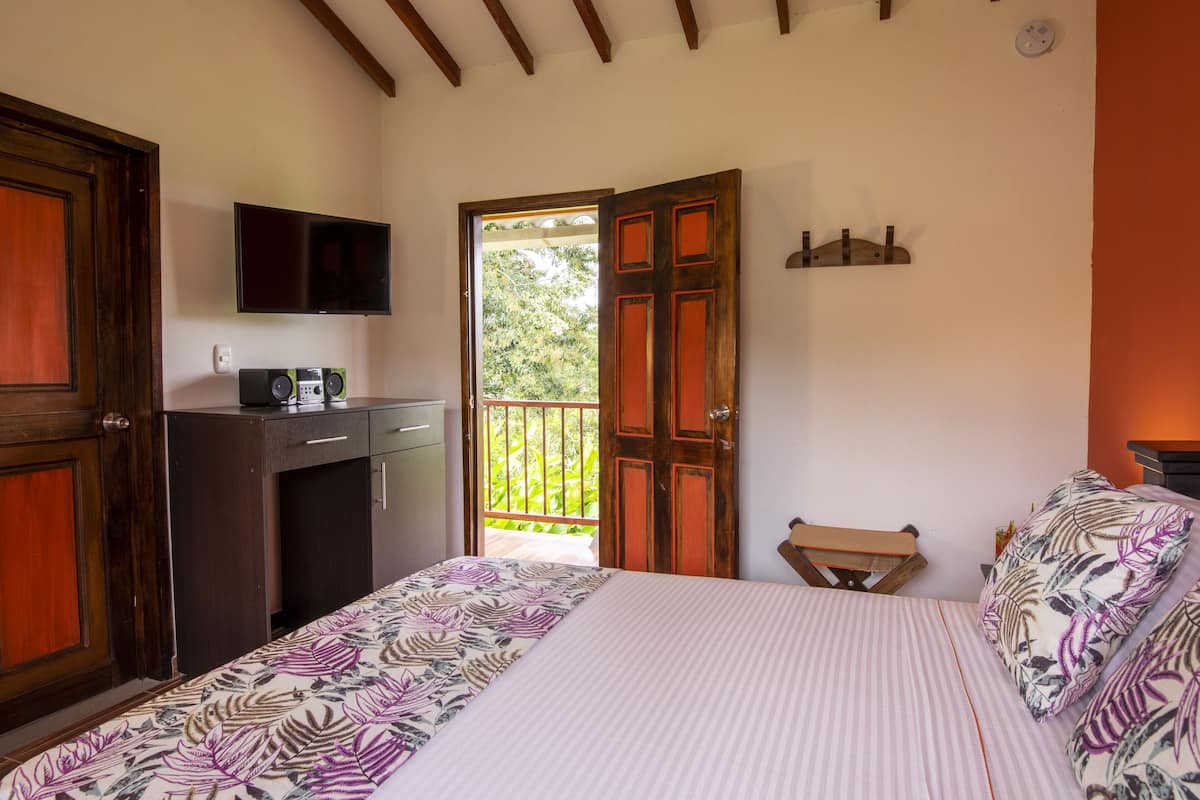 Ein Schlafzimmer mit Bett, Fernseher, Schreibtisch und Balkon.