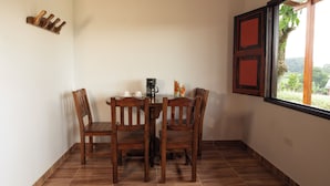 Un coin repas avec une table et des chaises en bois, une machine à café et une fenêtre donnant sur un paysage verdoyant.