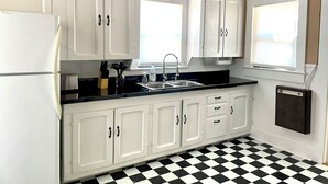Una cocina con armarios blancos, encimera negra, un lavabo y una ventana con persianas.