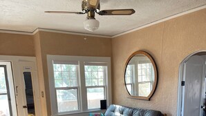 Una sala de estar con un sofá de cuero, una mesa de centro de madera, un ventilador de techo y un espejo grande en la pared.