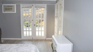 A bedroom with a bed, a dresser, a window with a view, and a door. - Mountain View Studio (Hemet)