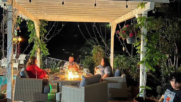 A covered outdoor seating area with wicker furniture, a fire feature, and hanging plants. - Mountain View Studio (Hemet)