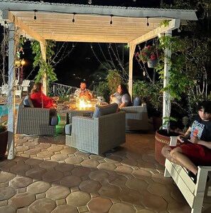 A covered outdoor seating area with wicker furniture, a fire feature, and hanging plants. - Mountain View Studio (Hemet)