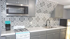 A kitchen with grey cabinets, a stainless steel microwave, a gas stove, and a sink. - Mountain View Studio (Hemet)