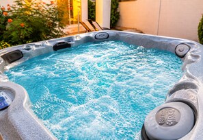 Un jacuzzi dont on peut voir le logo de la marque, entouré d’un jardin fleuri, avec un bâtiment en arrière-plan.