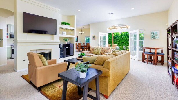 A spacious living room with a large sofa, a flat-screen TV mounted on the wall, a fireplace, and a dining area with chairs and a table. - 25% Off Sep 3-6! Perfect 4 Families -Pool, Jacuzzi (Palm Springs)