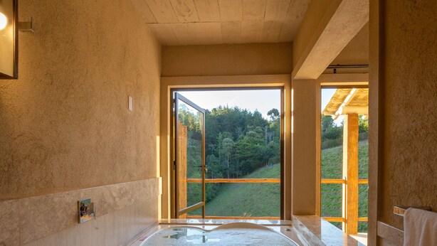 A bathroom with a large bathtub, a wooden ceiling, and a view of a green landscape through an open door. - Quinta dos Manacás Pousada (Venda Nova Do Imigrante)