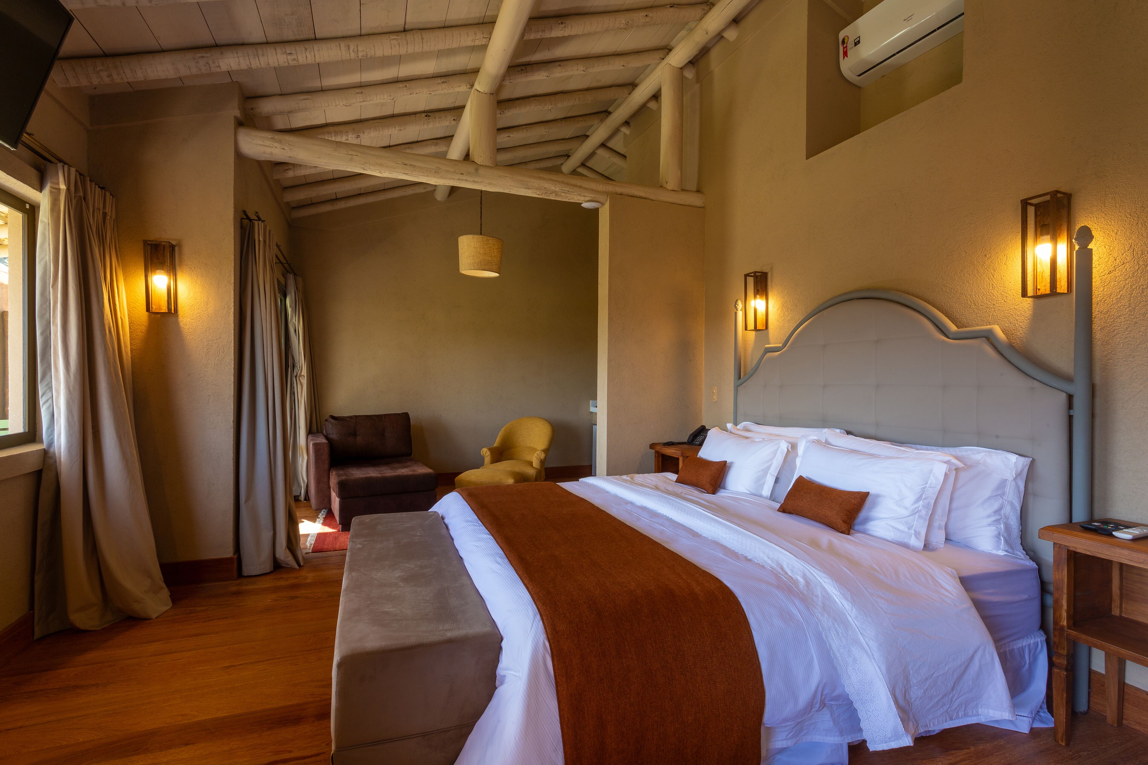 A hotel room with a large bed, a wooden ceiling, a chair, and a nightstand.