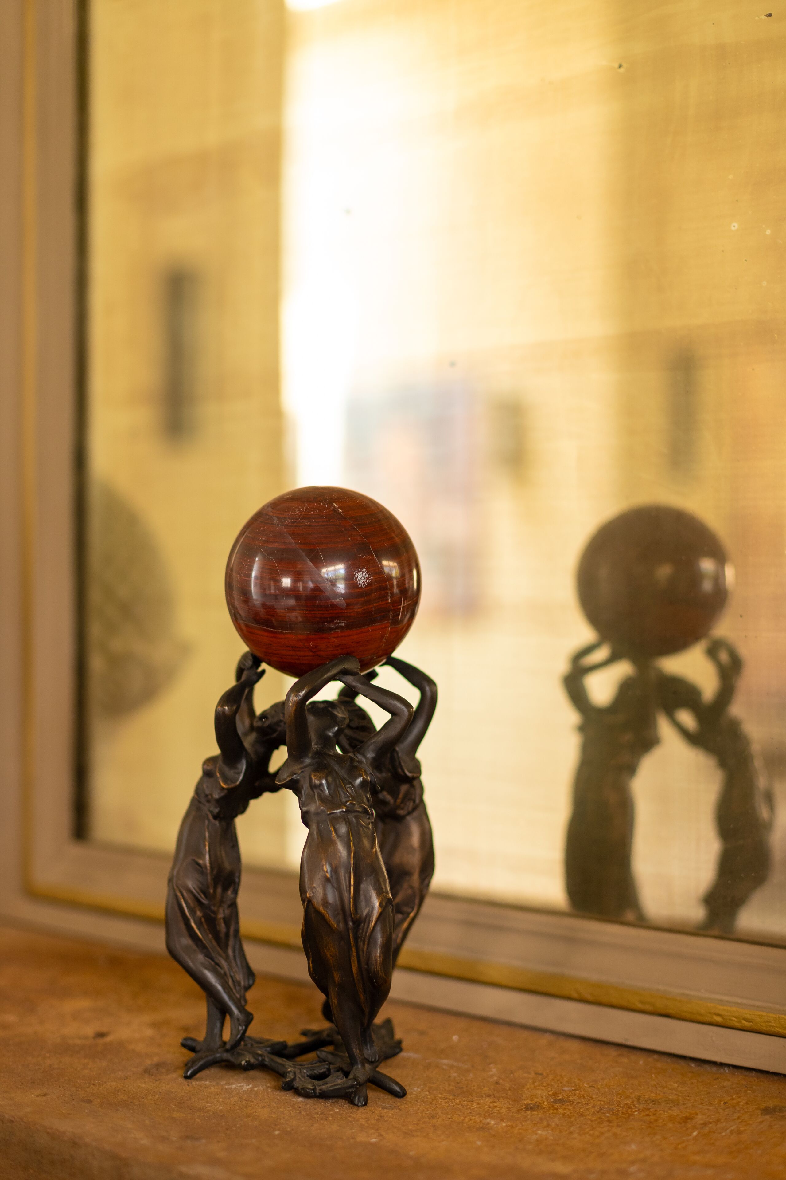 Escultura em bronze de duas figuras segurando uma esfera, colocada sobre uma superfície texturizada.
