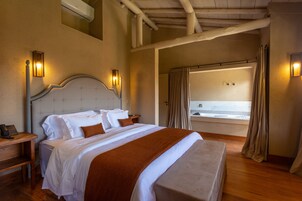 Quarto de hotel com uma cama grande, cabeceira de madeira, mesas de cabeceira e banheiro com banheira e chuveiro.