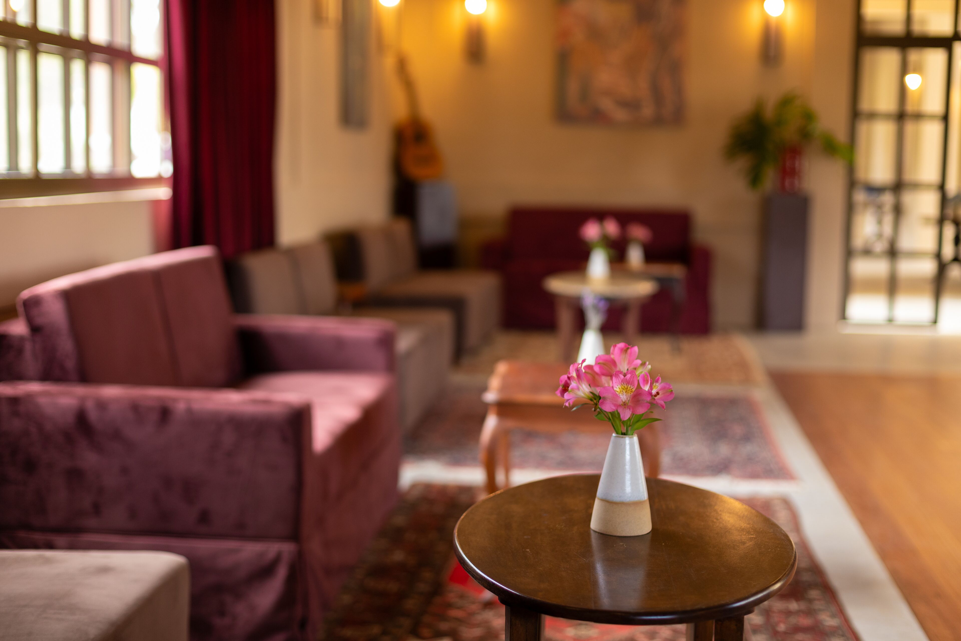 A modern lobby with a sofa, a round table with a vase of flowers, and a guitar in the background.