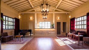 A spacious room with a wooden floor, a piano, sofas, and a large window. - Quinta dos Manacás Pousada (Venda Nova Do Imigrante)