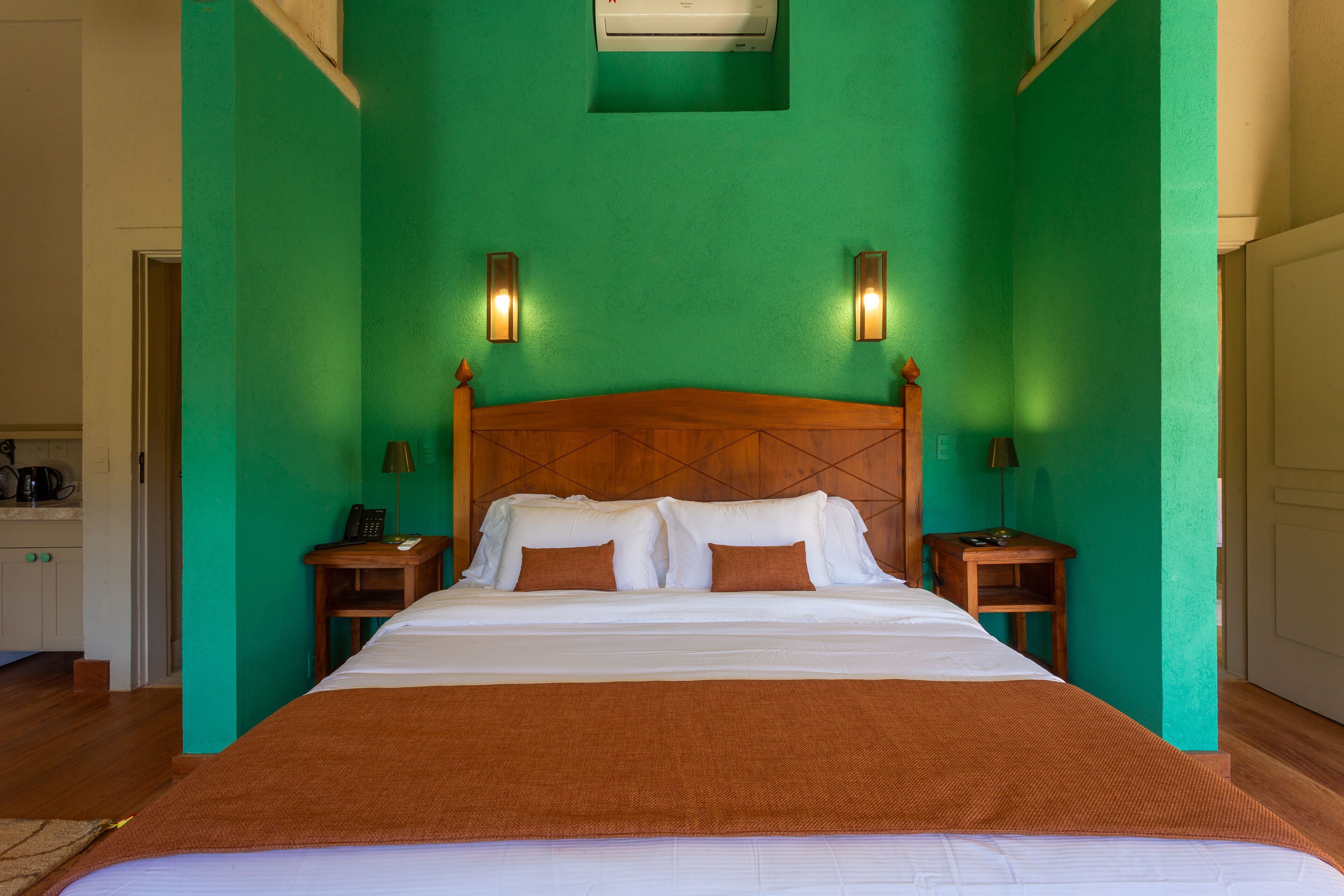 Una cama grande con cabecera de madera, dos mesitas de noche con lámparas y una pared verde.