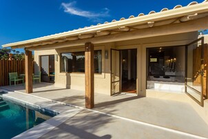 Uma área moderna de piscina ao ar livre com pérgola, deck de madeira e céu azul claro.