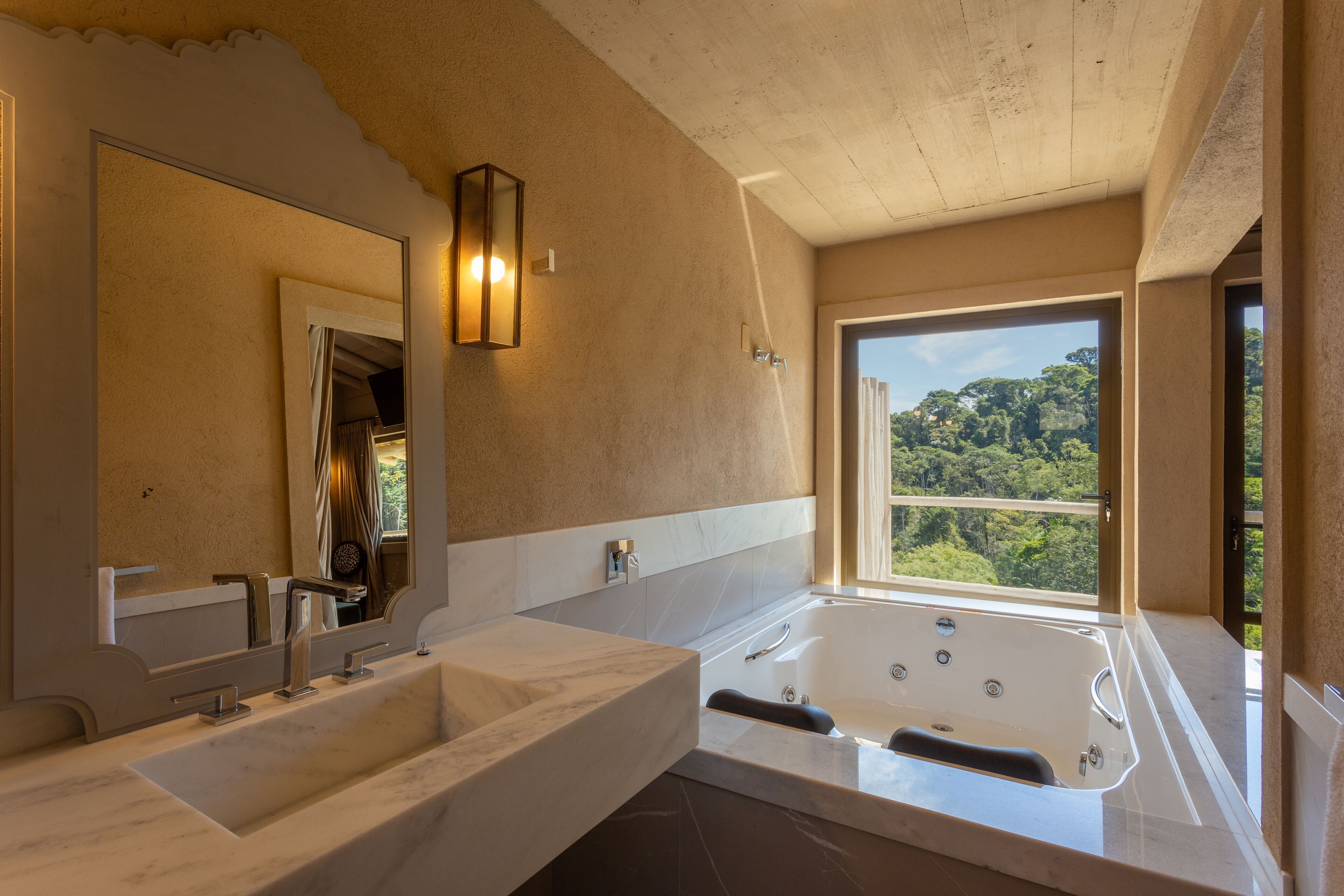 A bathroom with a large bathtub, a double sink, and a large mirror. There is a window providing a view of the outdoors.