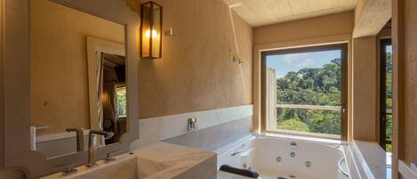 A bathroom with a large bathtub, a double sink, and a large mirror. There is a window providing a view of the outdoors.