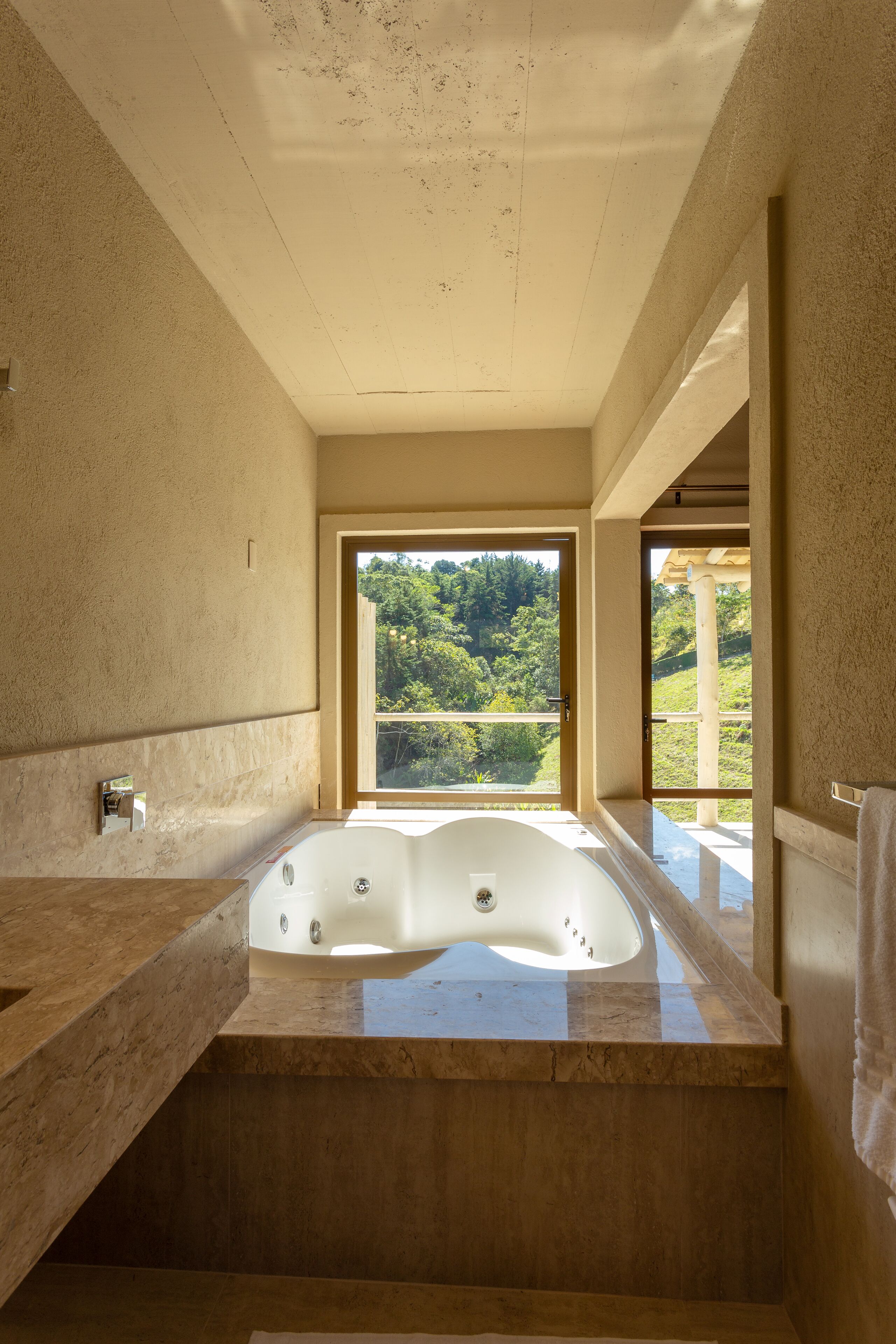 Un baño moderno con una bañera grande, un tocador de madera y vistas a un exuberante follaje exterior.